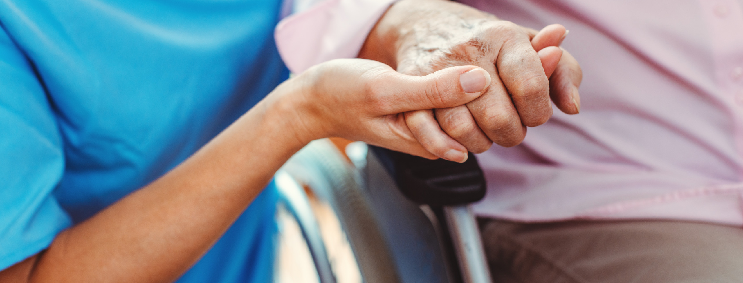 Vårdpersonal som håller rullstolsburen person i handen