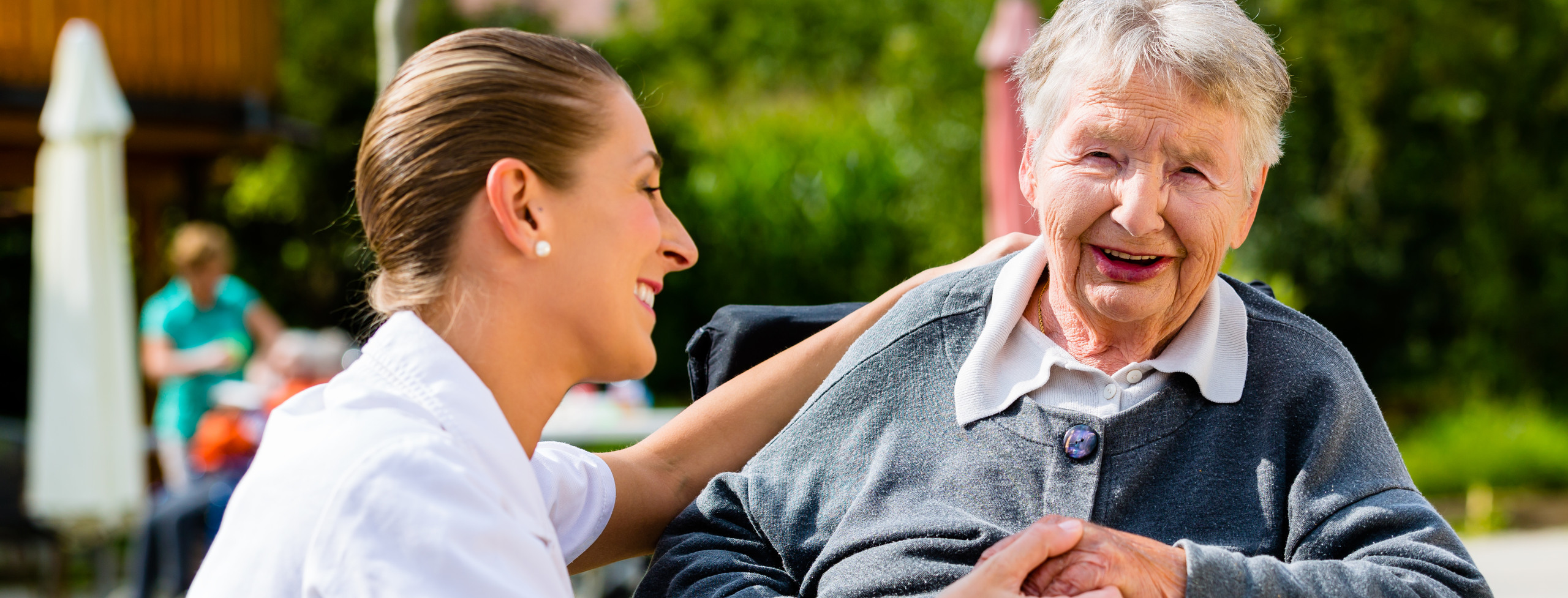 Äldre kvinna i rullstol med en yngre omsorgsgivare sittande till höger om kvinnan.