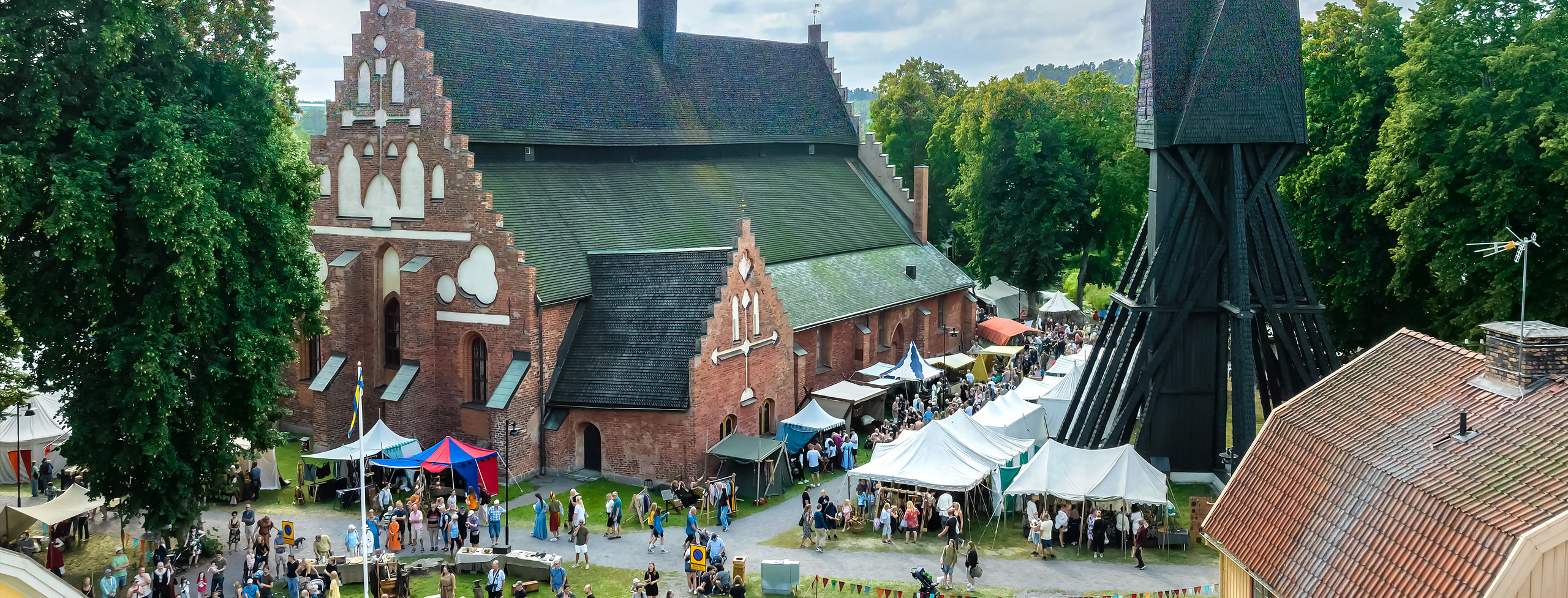 Bild visar Sankt Laurentii kyrka och klockstapel med Gästabudsbesökare framför