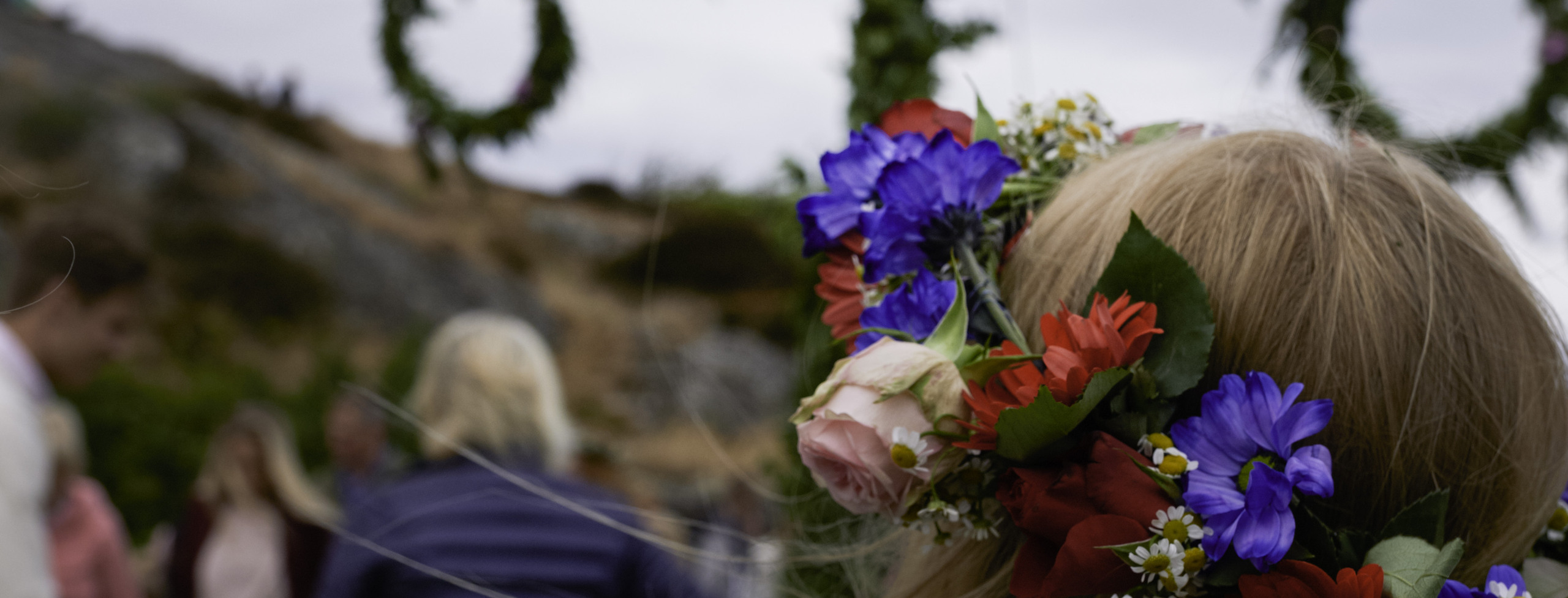 Bild visar en flicka i midsommarkrans framför en midsommarstång