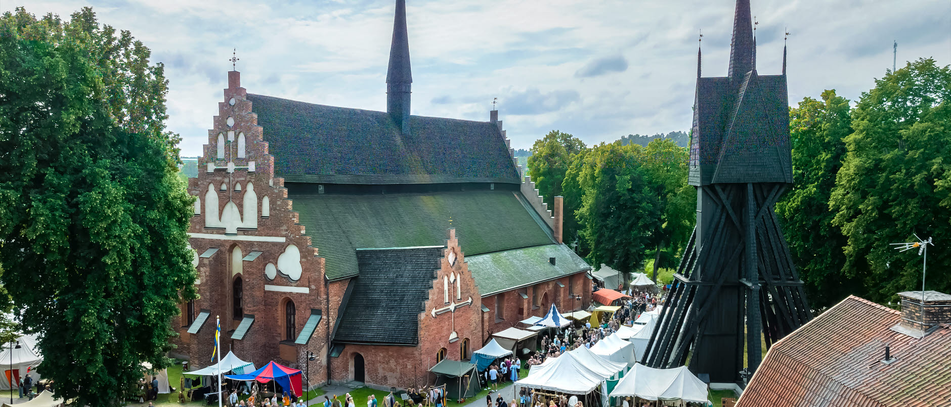 Bild visar Sankt Laurentii kyrka och klockstapel med Gästabudsbesökare framför