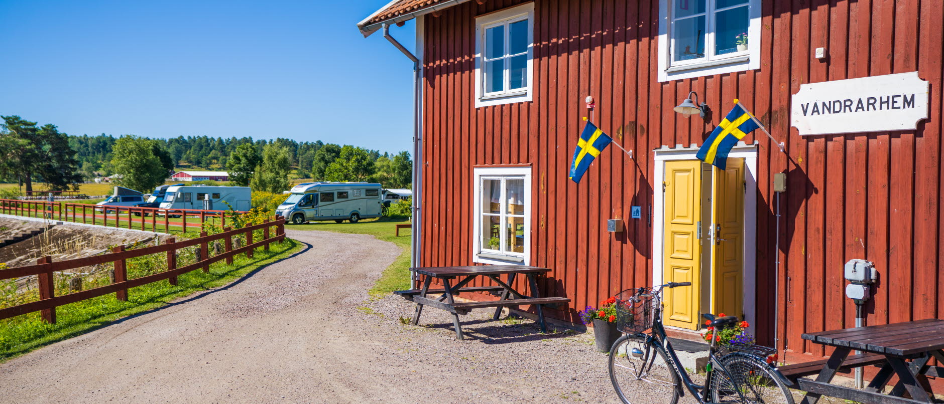 Foto: Bild visar Skeppsdockans camping. Ett rött hus med vandrarhem i förgrunder och husbilar i bakgrunden