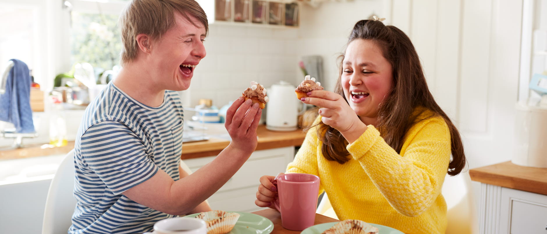 En glad kvinna med mörkt långt hår tittar på en skärm tillsammans med en man i randig tröja.